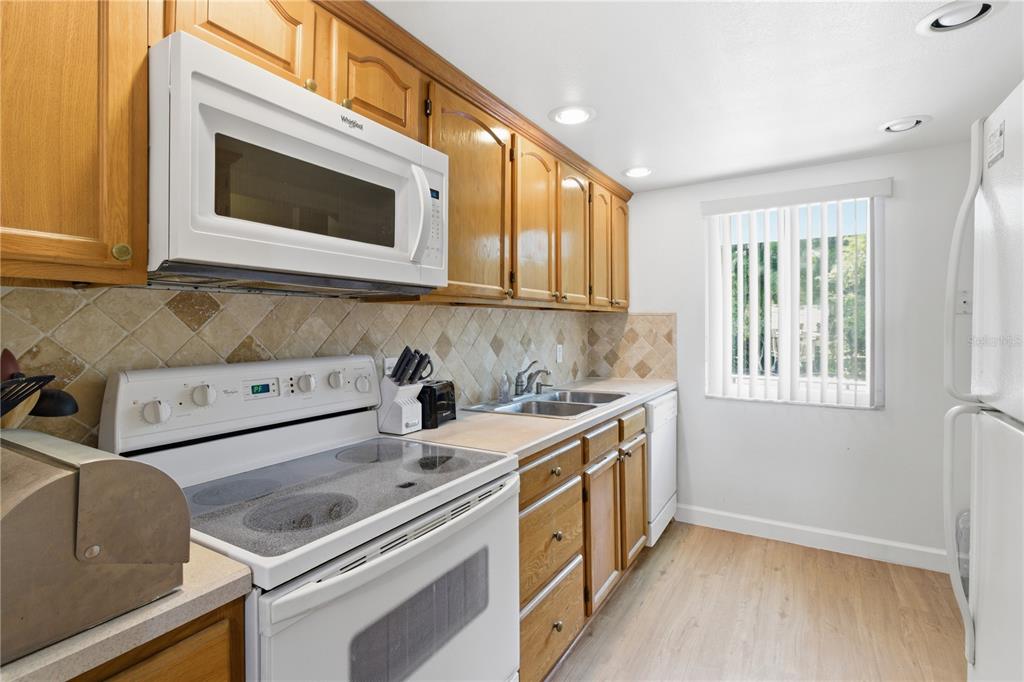 A kitchen features wood cabinets, white appliances, a tiled backsplash, and light-colored flooring — 2060 MARILYN STREET UNIT 207, CLEARWATER, FL