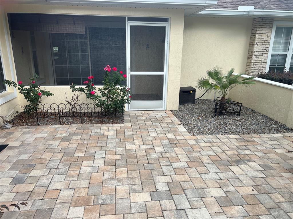 A paved patio features a screened door, rose bushes, and a small palm tree — 6847 SW 114TH STREET ROAD, OCALA, FL