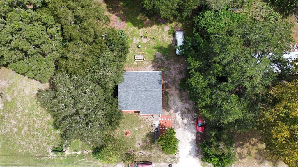 An aerial view shows a house with a gray roof surrounded by trees and vehicles — 6415 NE 23RD AVENUE, OCALA, FL