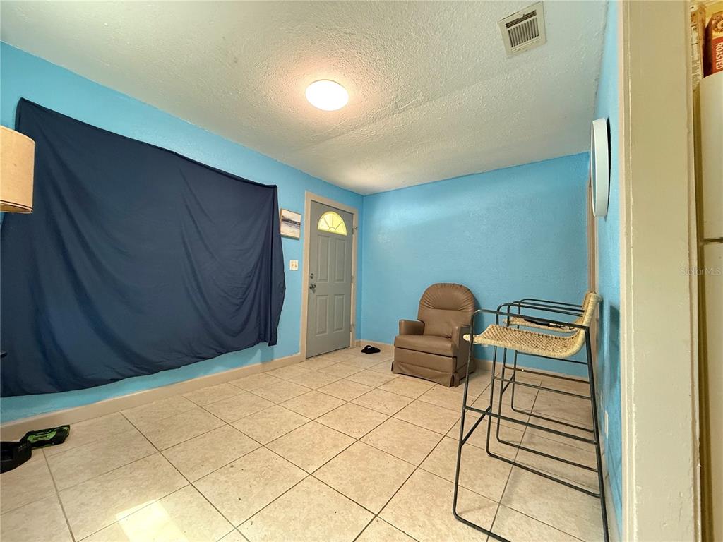 A room with light blue walls, tiled flooring, a front door, and a recliner chair — 6415 NE 23RD AVENUE, OCALA, FL