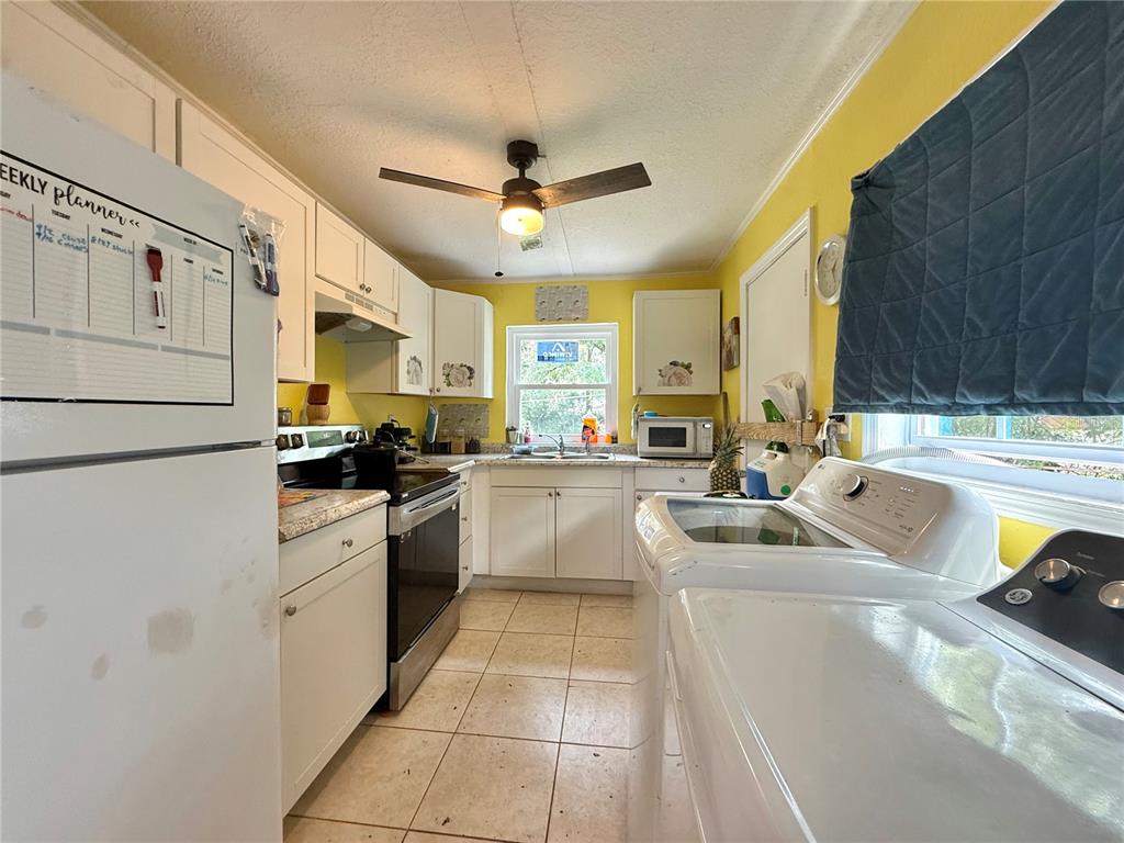 A kitchen with white cabinets, yellow walls, tile flooring, and a laundry area — 6415 NE 23RD AVENUE, OCALA, FL