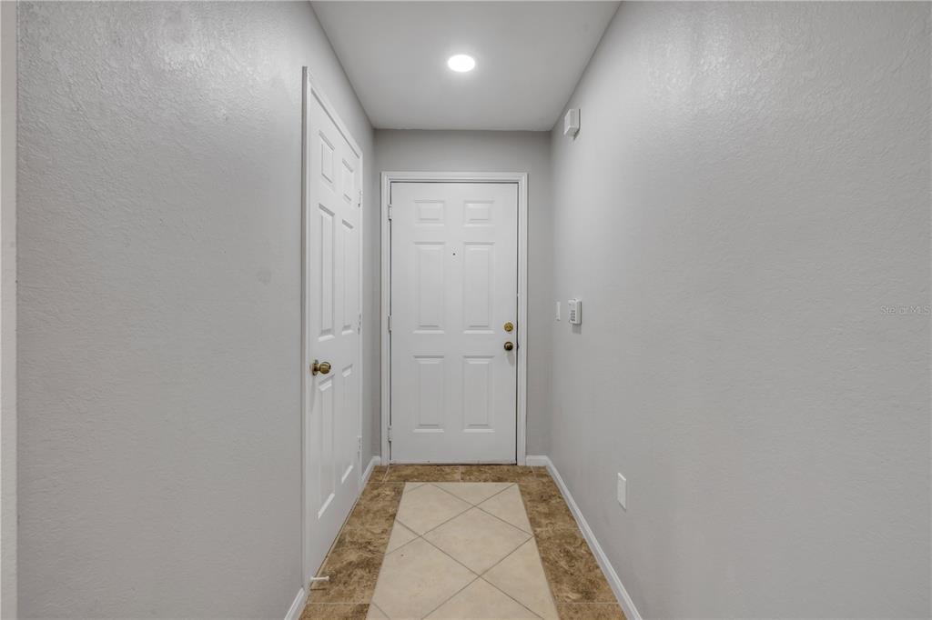 A small entryway features light gray walls, a white front door, and tiled flooring — 940 VILLAGE TRAIL UNIT 4-306, PORT ORANGE, FL