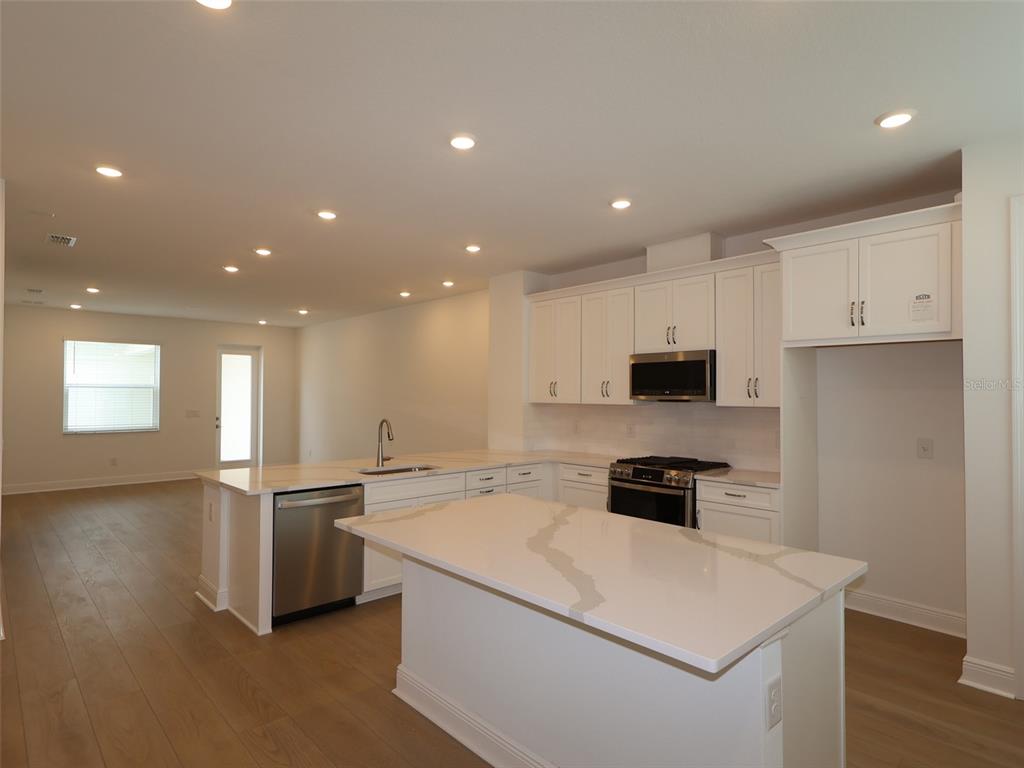 A modern kitchen features white cabinetry, quartz countertops, a center island, and stainless steel appliances — 4458 SUNSET GARDEN STREET, BRADENTON, FL