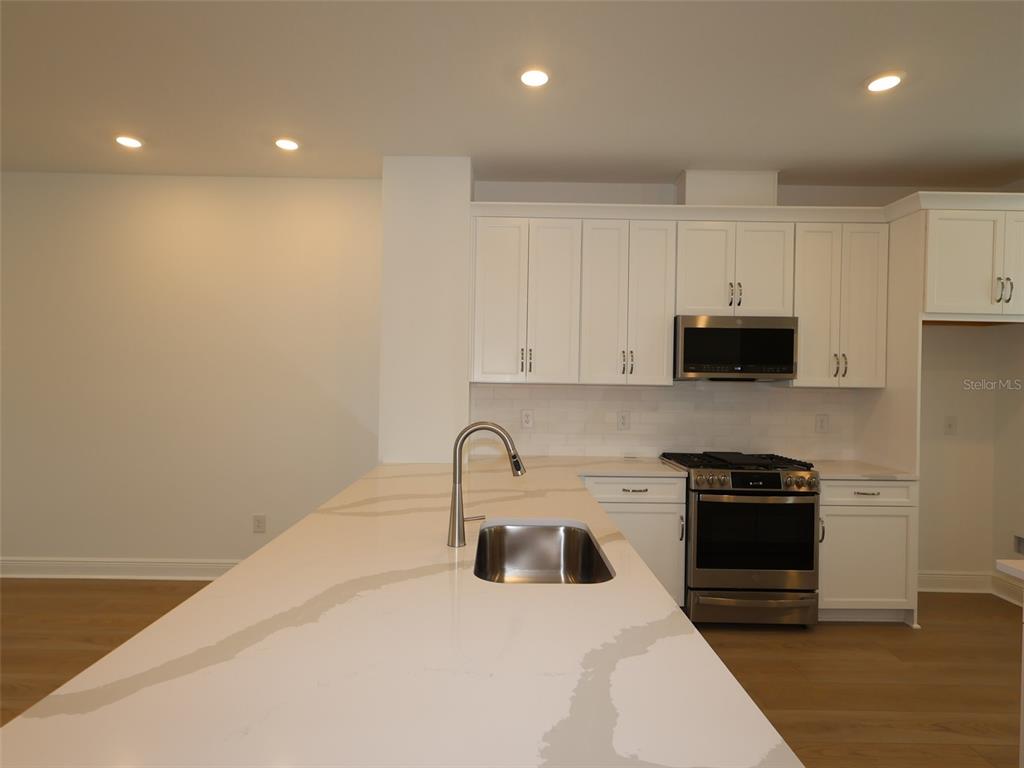 A modern kitchen features a large white quartz island, white cabinetry, and stainless steel appliances — 4458 SUNSET GARDEN STREET, BRADENTON, FL