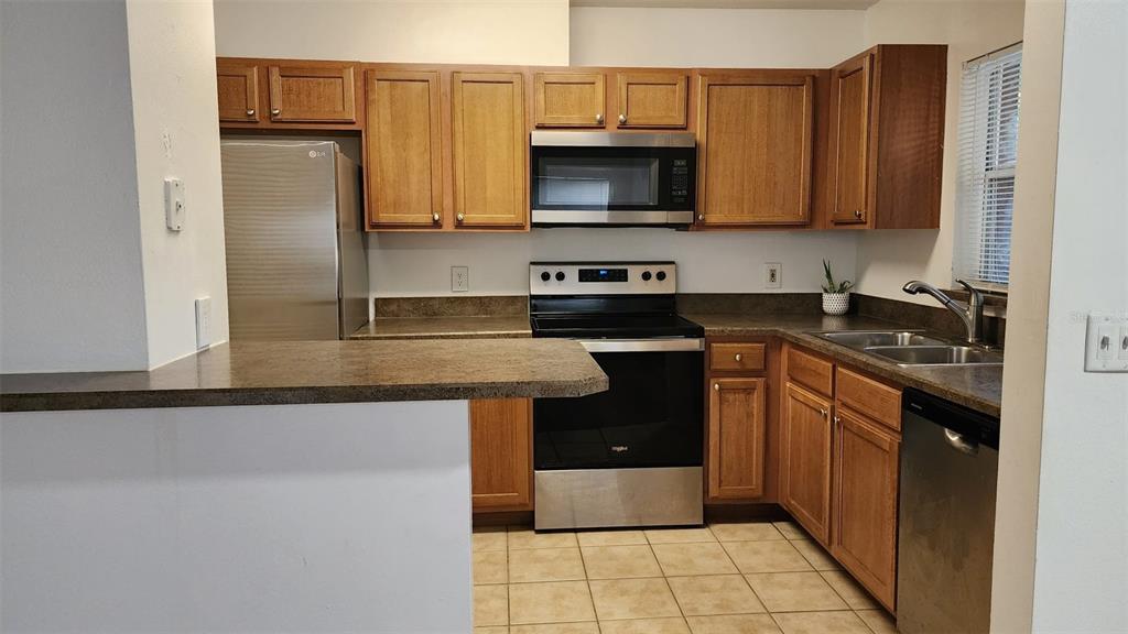 A kitchen features wood cabinets, stainless steel appliances, a breakfast bar, and tile flooring — 5436 E MICHIGAN STREET UNIT 5436-3, ORLANDO, FL