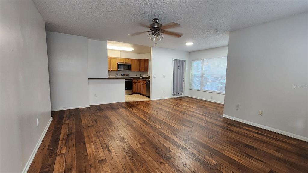 An open-concept living room features wood-look flooring, a ceiling fan, and an adjacent kitchen — 5436 E MICHIGAN STREET UNIT 5436-3, ORLANDO, FL