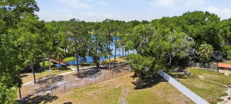 An aerial view shows a fenced backyard with trees leading to a lake and bridge — 5345 AVON COURT, ORLANDO, FL