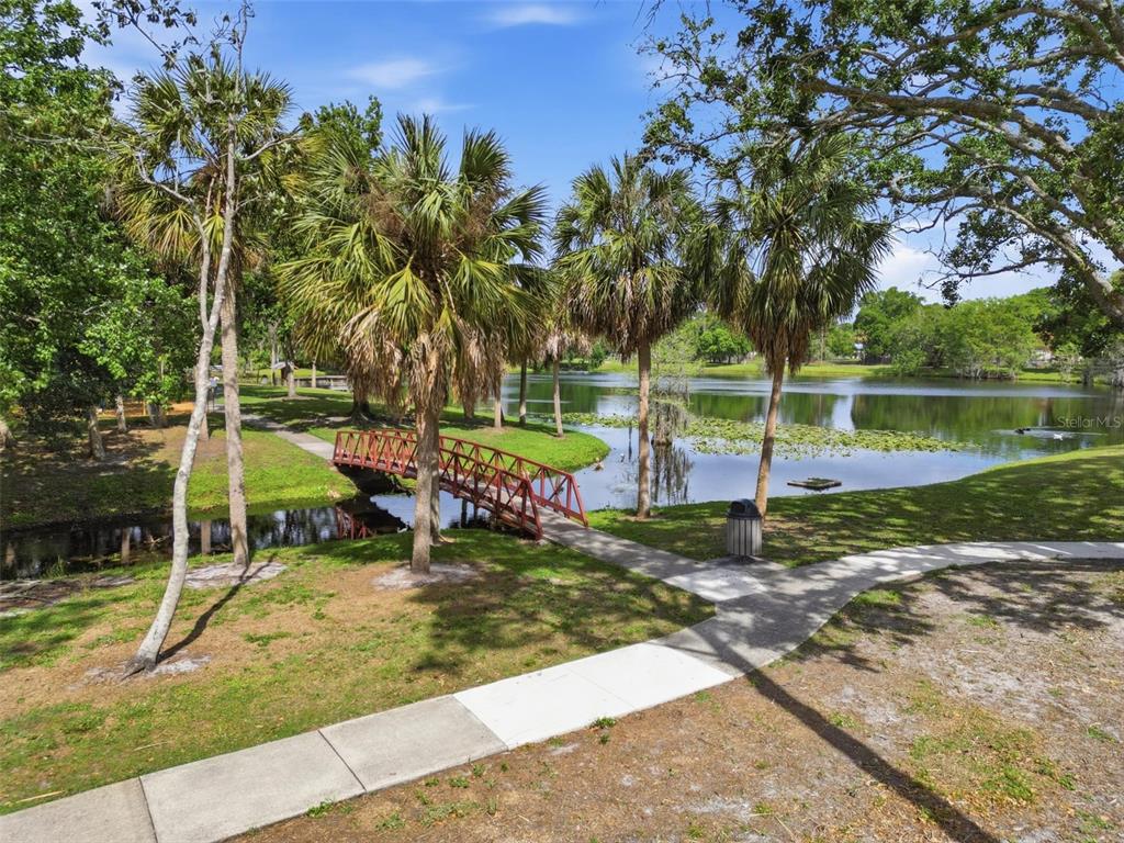 A red footbridge crosses a small stream in a park with palm trees and a lake — 5345 AVON COURT, ORLANDO, FL