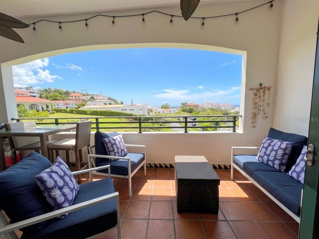 A covered balcony with outdoor furniture overlooks a grassy landscape and distant buildings — 6000 BLVD RIO MAR UNIT 7105, RIO GRANDE, PR