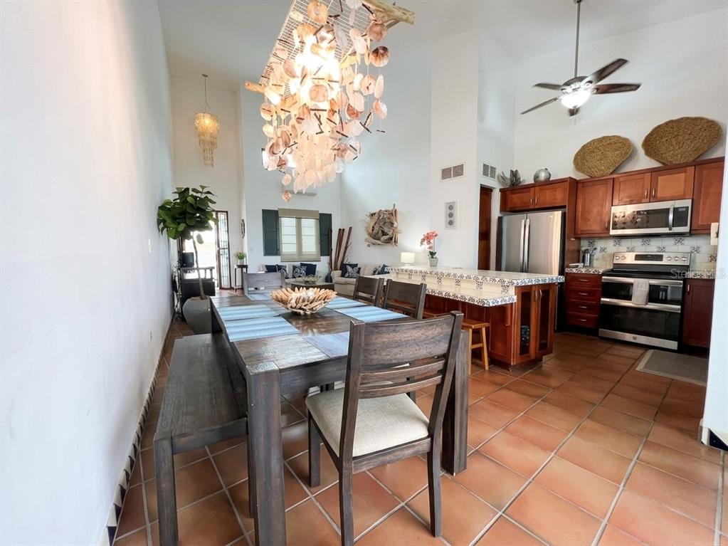 A dining area and kitchen feature tile floors, wooden furniture, and a shell chandelier — 6000 BLVD RIO MAR UNIT 7105, RIO GRANDE, PR