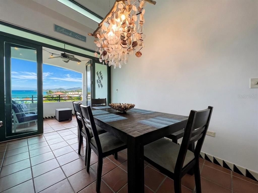 A dining room features a dark wood table, shell chandelier, and a balcony with ocean views — 6000 BLVD RIO MAR UNIT 7105, RIO GRANDE, PR