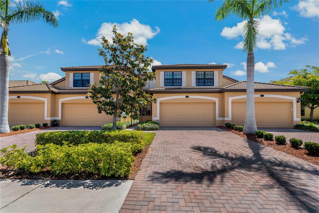 A multi-unit residential building with beige stucco, tiled roofs, and paved driveways — 7015 GRAND ESTUARY TRAIL UNIT 103, BRADENTON, FL