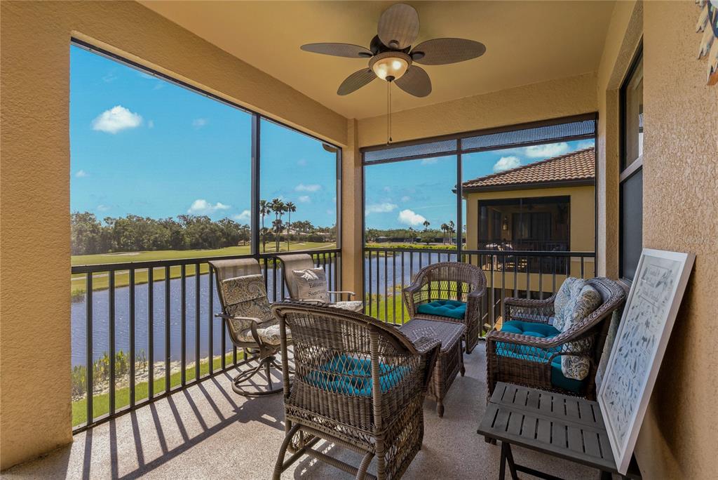 A screened-in balcony with wicker furniture overlooks a pond and a golf course — 7015 GRAND ESTUARY TRAIL UNIT 103, BRADENTON, FL