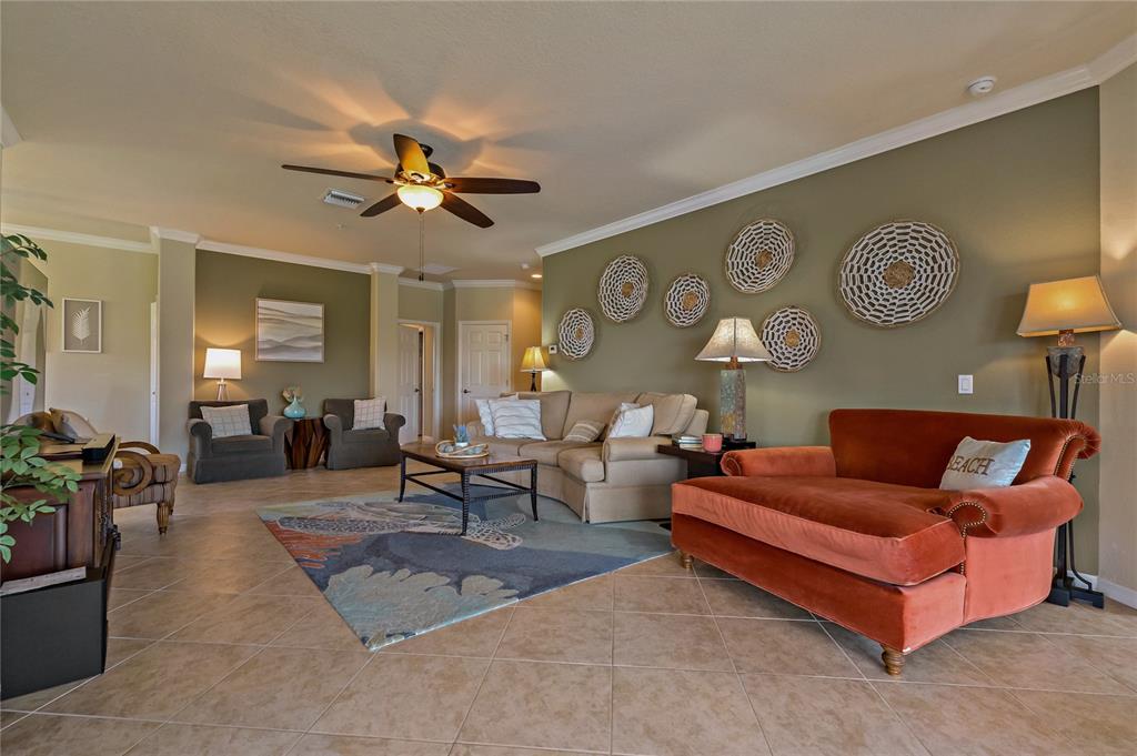 A living room features tile floors, a ceiling fan, and a large orange velvet chaise — 7015 GRAND ESTUARY TRAIL UNIT 103, BRADENTON, FL