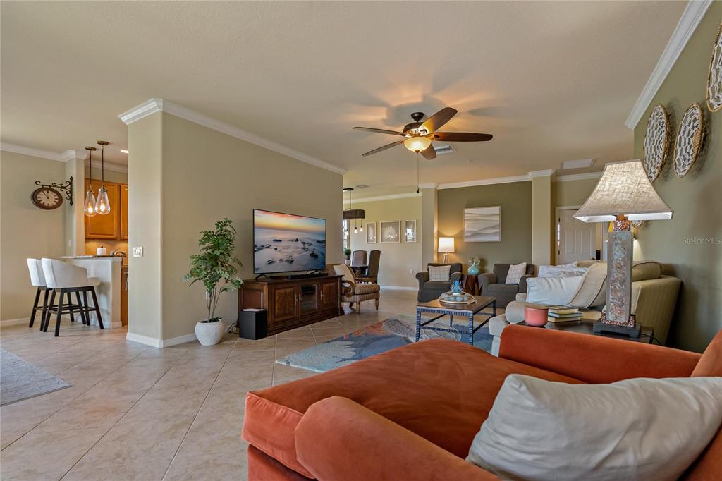 An open-concept living room features tile flooring, a television, and an orange sofa — 7015 GRAND ESTUARY TRAIL UNIT 103, BRADENTON, FL