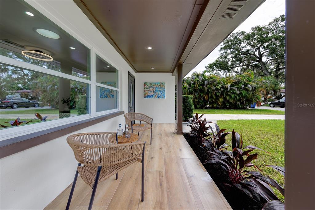 A covered front porch features wood-look flooring, two woven chairs, and a small side table — 3042 KAPOK KOVE DRIVE, CLEARWATER, FL