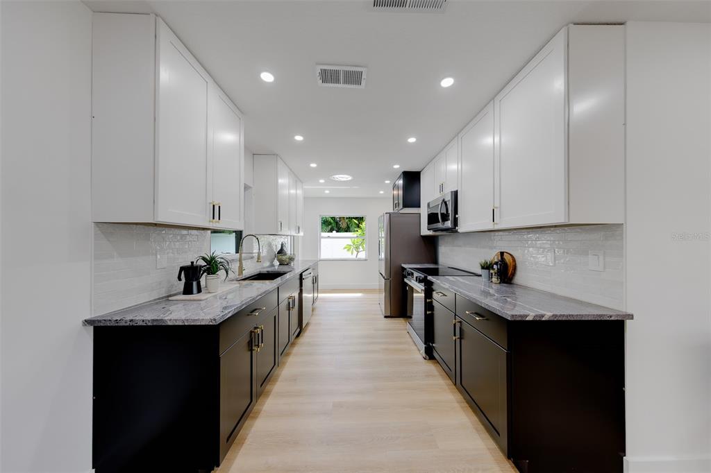 A galley kitchen features white upper cabinets, dark lower cabinets, granite countertops, and stainless appliances — 3042 KAPOK KOVE DRIVE, CLEARWATER, FL
