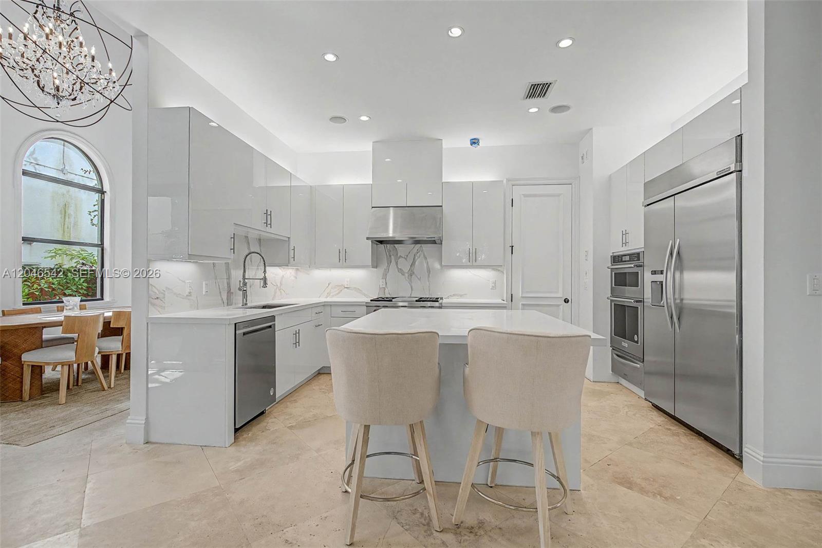 A modern white kitchen features an island with bar stools and stainless steel appliances — 2561 Trapp Ave, Miami FL 33133, MIAMI, FL