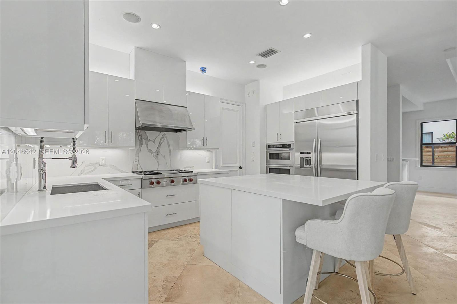 A modern white kitchen features marble backsplashes, stainless steel appliances, and a central island — 2561 Trapp Ave, Miami FL 33133, MIAMI, FL