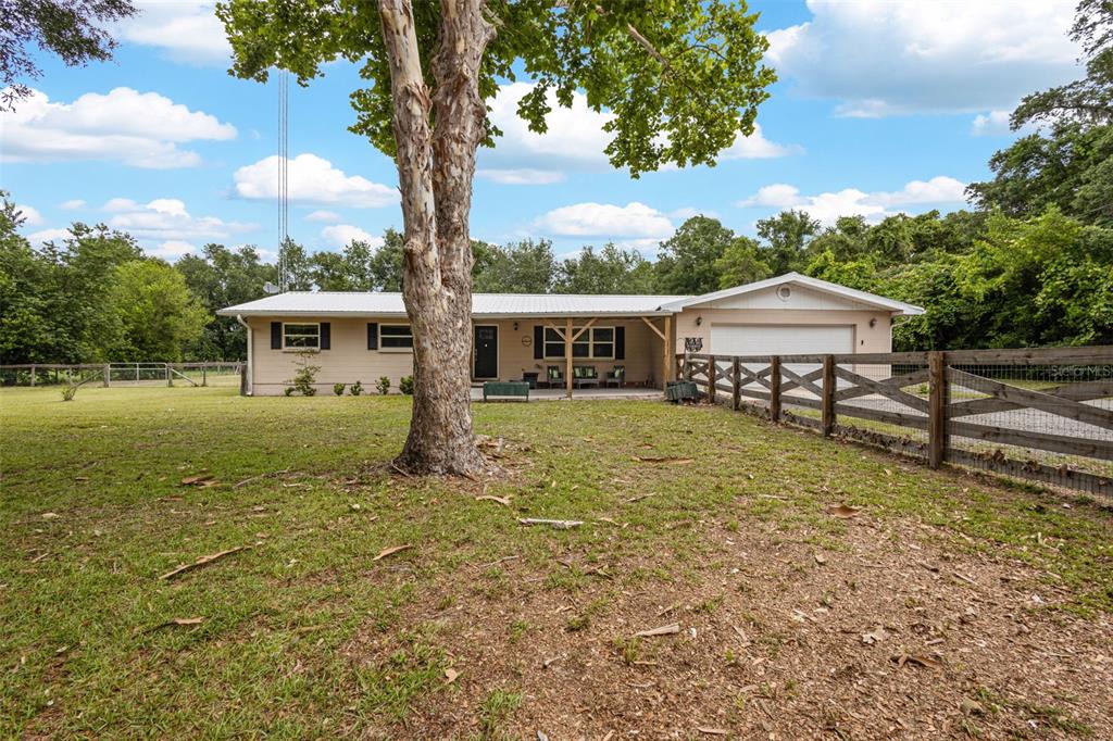 A single-story house with a metal roof, attached garage, and a wooden fence in front — 7251 NW 40TH STREET, CHIEFLAND, FL
