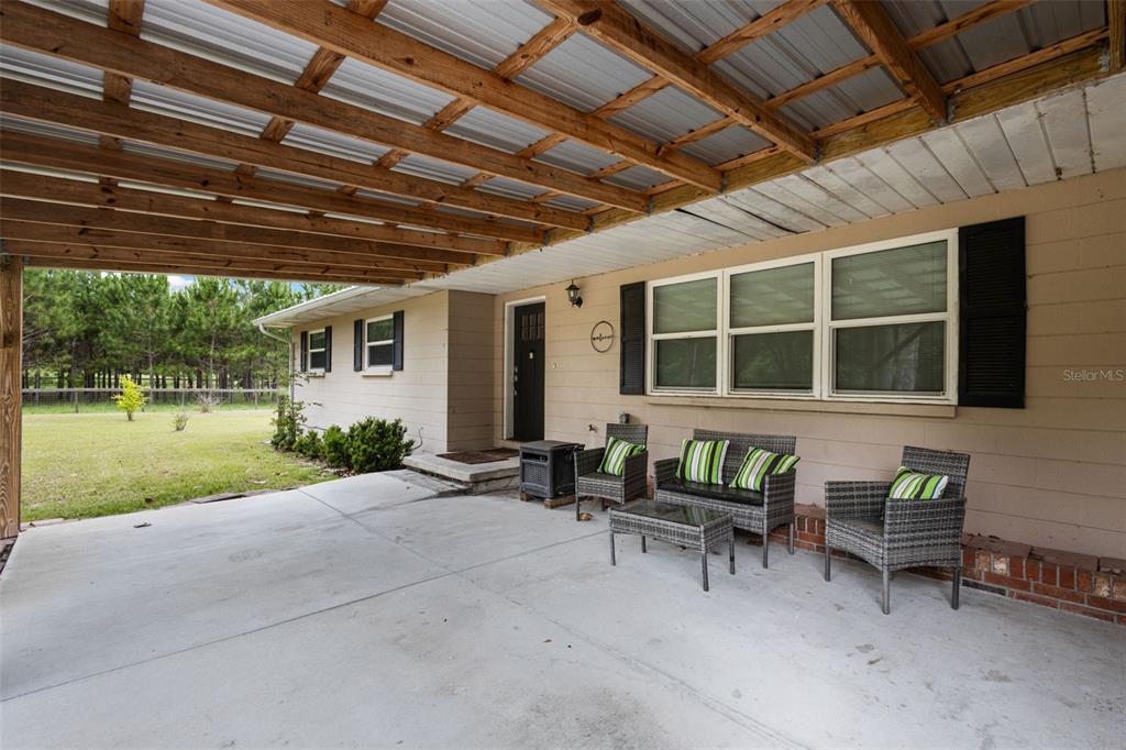A covered concrete patio features outdoor furniture in front of a tan house exterior — 7251 NW 40TH STREET, CHIEFLAND, FL