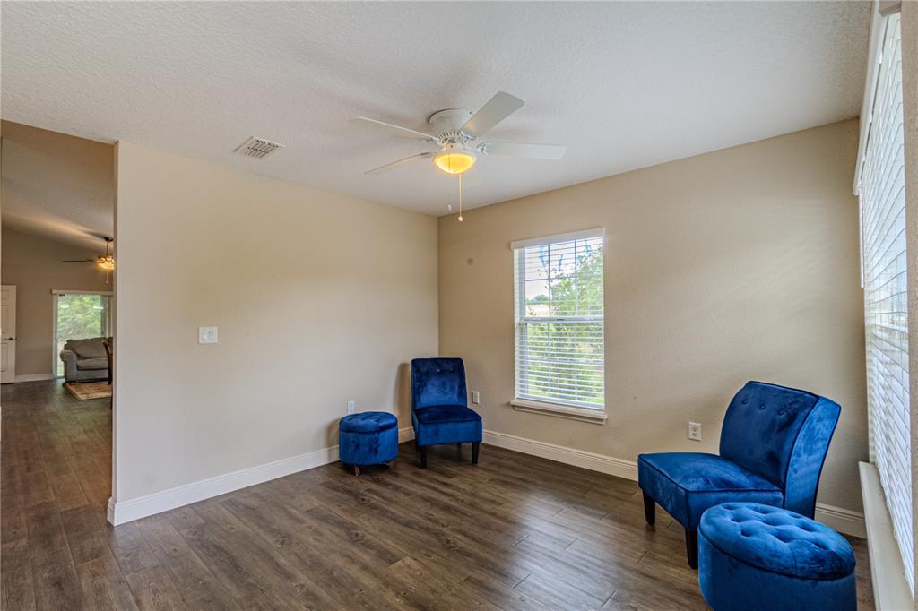 A room with wood-look flooring, two blue velvet chairs, two matching ottomans, and a ceiling fan — 8593 PLUMERIA AVENUE, ORLANDO, FL