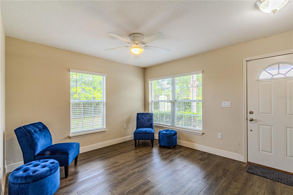 A room with wood-look flooring, two blue velvet chairs, two ottomans, and a ceiling fan — 8593 PLUMERIA AVENUE, ORLANDO, FL