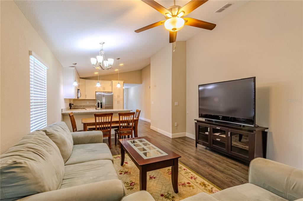 An open-concept living and dining area features a sofa, coffee table, television, and kitchen — 8593 PLUMERIA AVENUE, ORLANDO, FL