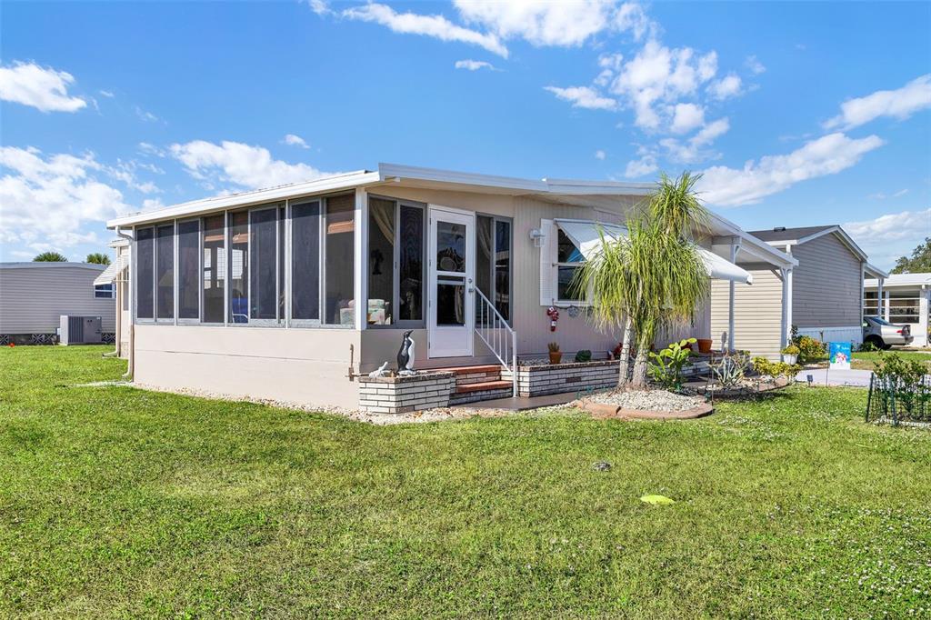 A single-story mobile home features a screened-in porch, brick accents, and a palm tree — 220 LA ROSAS, NORTH PORT, FL