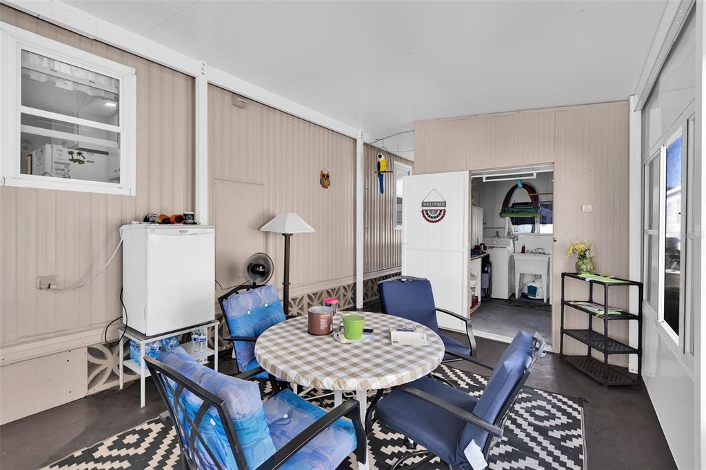 A covered patio features a round table with four chairs, a mini-fridge, and a doorway — 220 LA ROSAS, NORTH PORT, FL