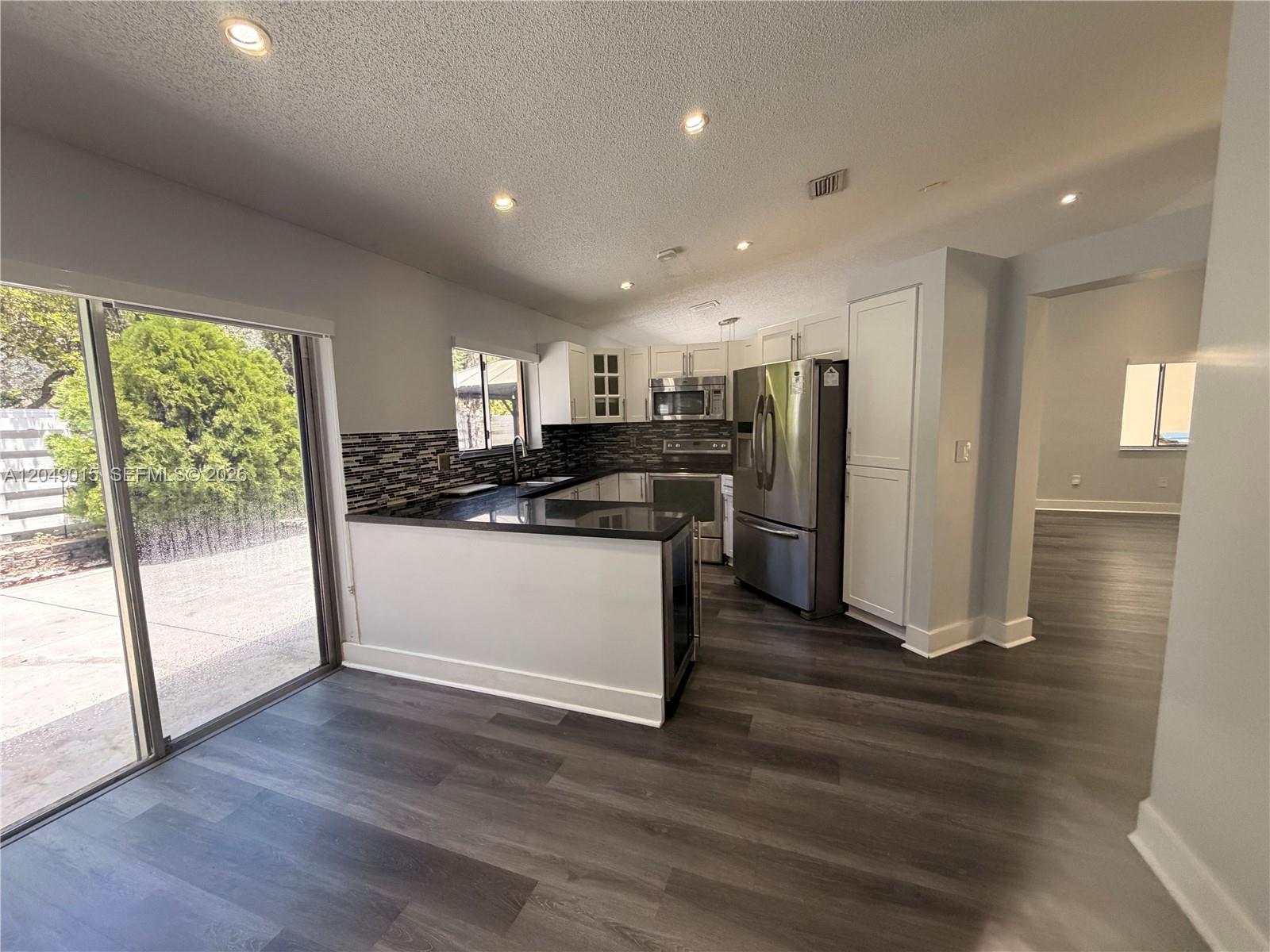 A kitchen features white cabinetry, stainless steel appliances, a black countertop, and dark wood flooring — 14467 SW 137th Ct, Miami FL 33186, MIAMI, FL