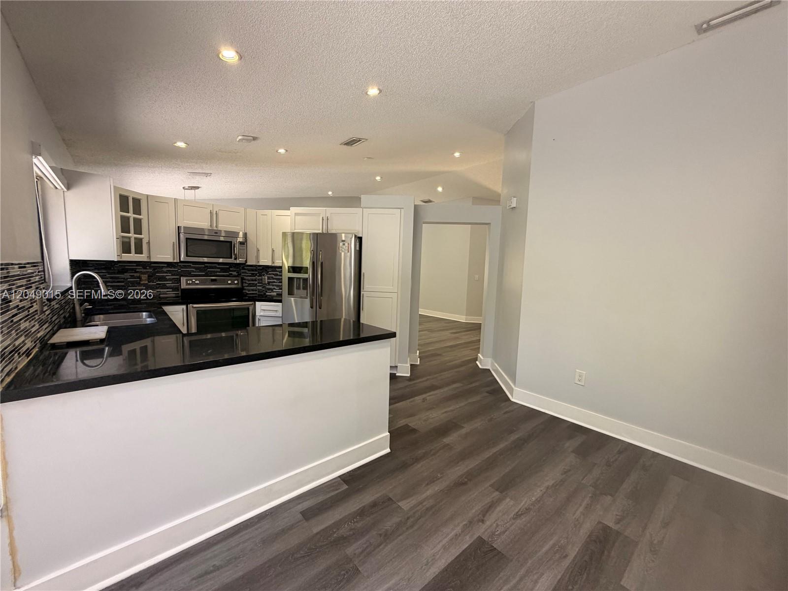 A kitchen features white cabinets, black countertops, stainless steel appliances, and dark wood-look flooring — 14467 SW 137th Ct, Miami FL 33186, MIAMI, FL