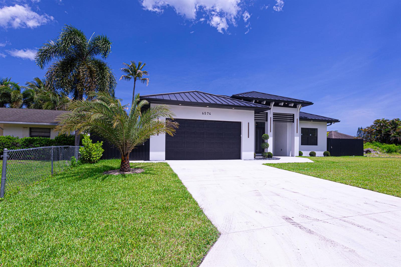 A modern single-story house with a black garage door, metal roof, and palm trees — 6574 Rigger Road, Lake Worth FL 33462, LAKE WORTH, FL
