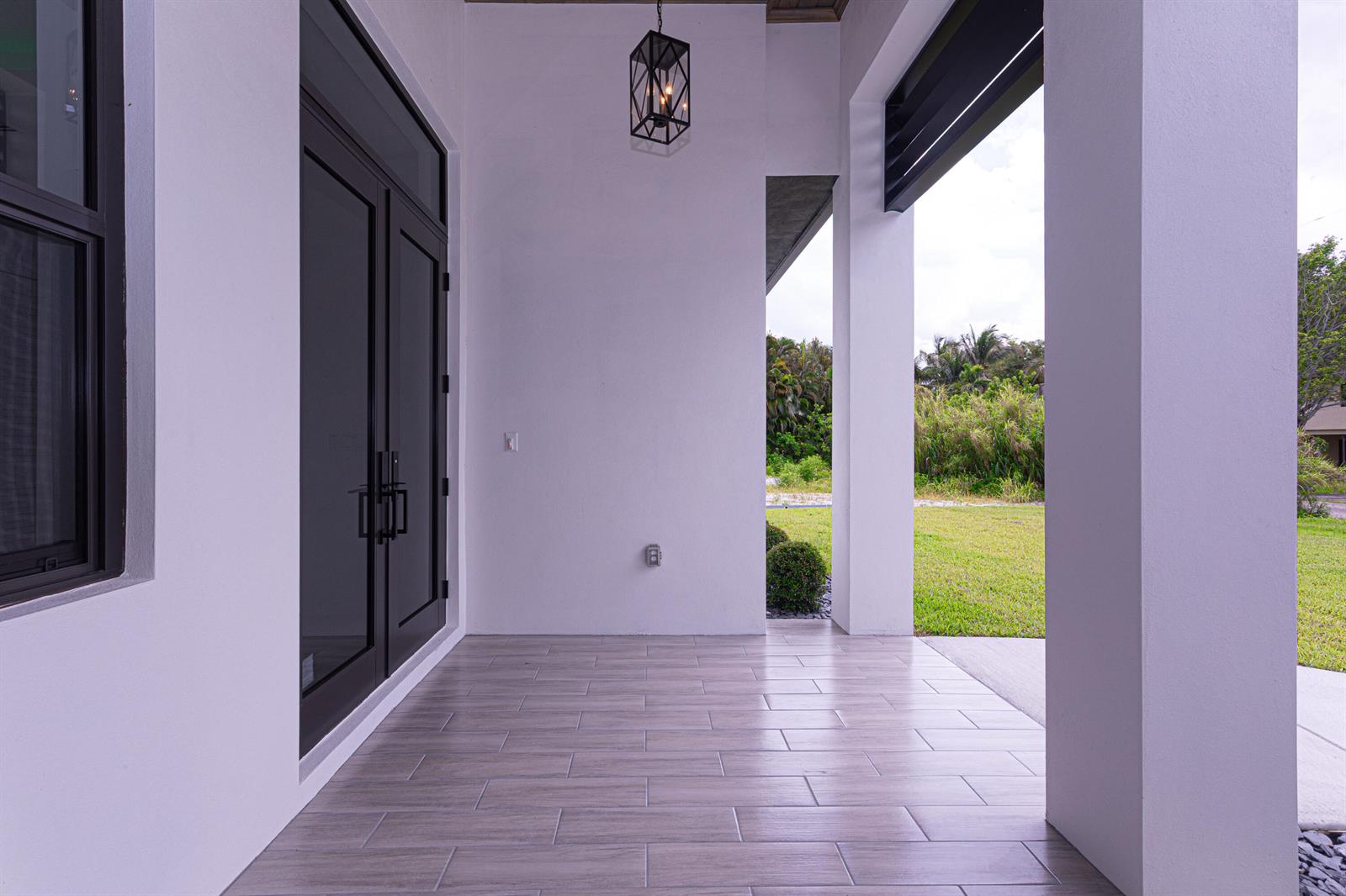 A covered porch features light wood-look tile flooring, white walls, and a black lantern pendant — 6574 Rigger Road, Lake Worth FL 33462, LAKE WORTH, FL