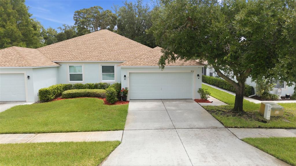 A light blue single-story house features a two-car garage, a shingled roof, and manicured landscaping — 5852 AUTUMN SHIRE, ZEPHYRHILLS, FL