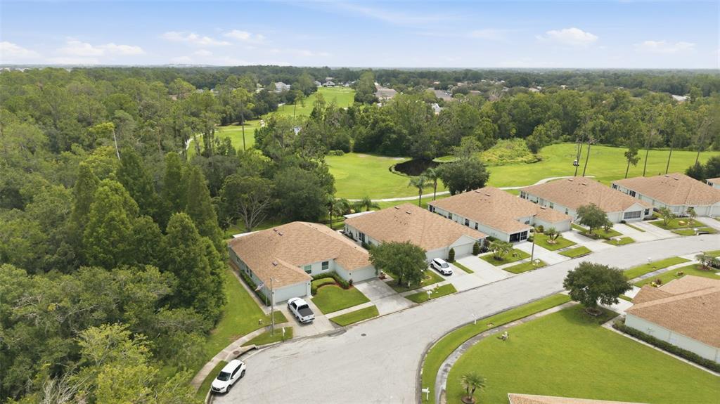 An aerial view shows a suburban street with houses bordering a golf course and woods — 5852 AUTUMN SHIRE, ZEPHYRHILLS, FL