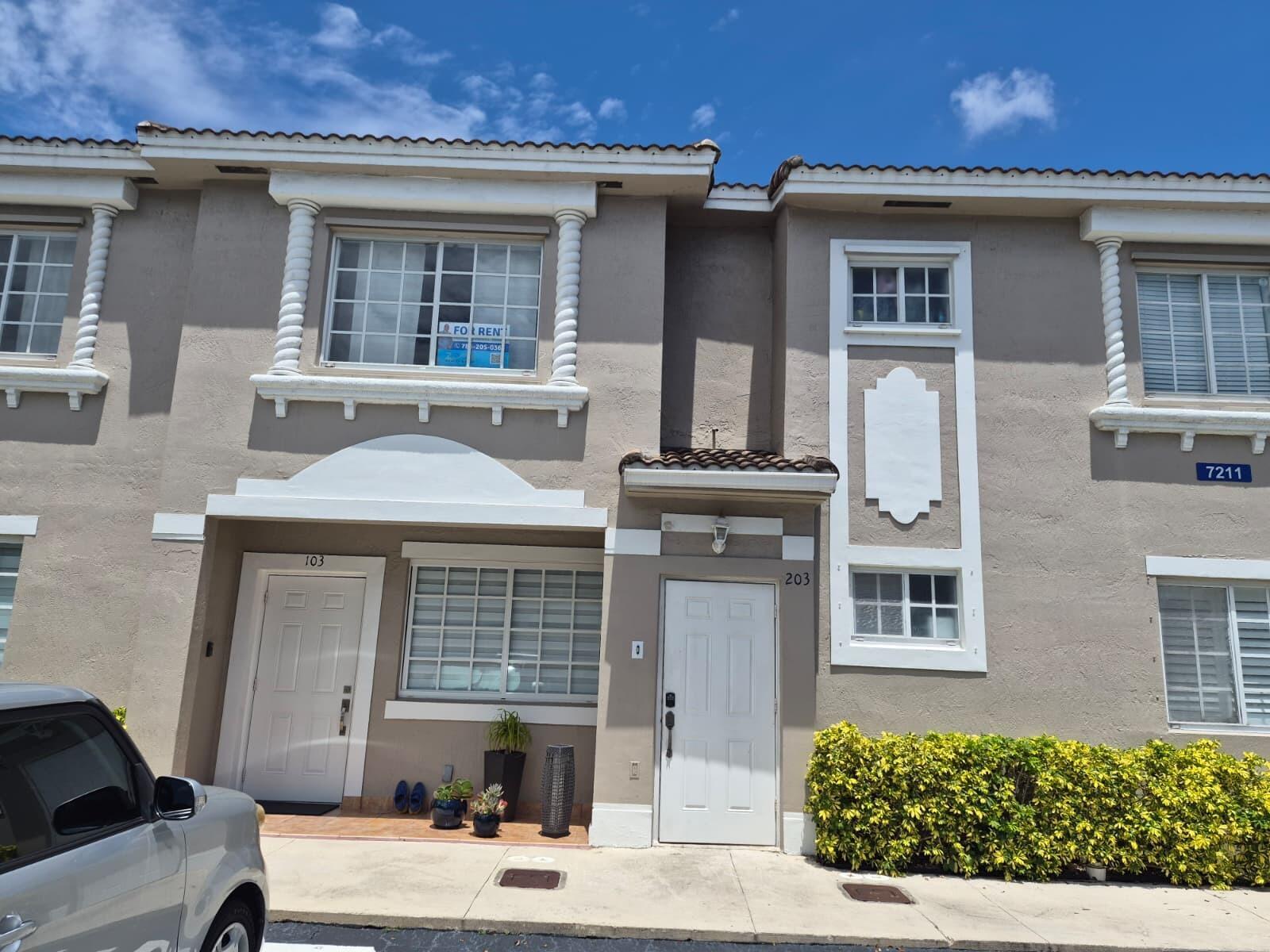 The exterior of a two-story townhouse complex features beige stucco walls and white trim — 7211 NW 174th Terrace # 203, Hialeah FL 33015, HIALEAH, FL