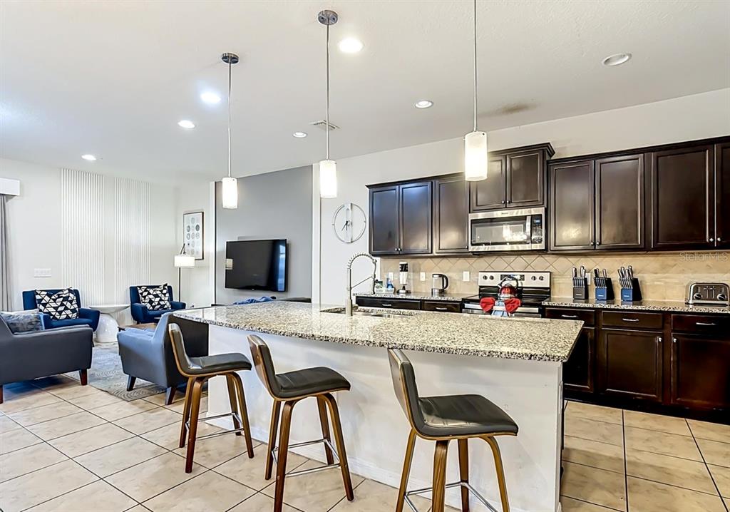 A kitchen with dark cabinets and granite countertops features a large island with bar seating — 1603 LIMA AVENUE, KISSIMMEE, FL