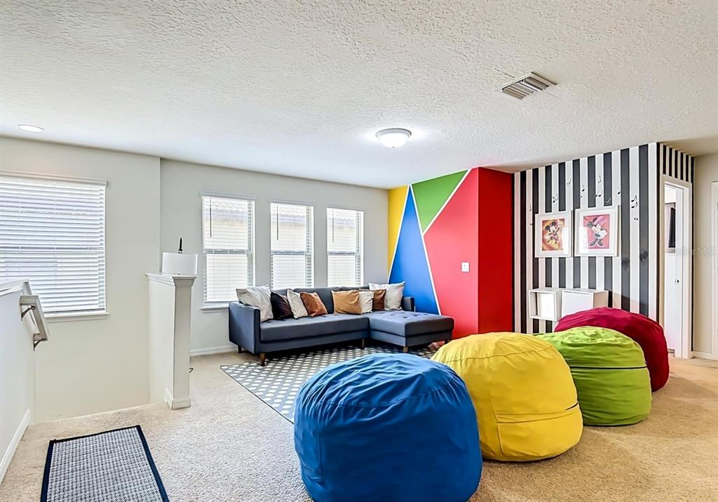 A carpeted loft features a gray sectional sofa, three colorful beanbag chairs, and a striped wall — 1603 LIMA AVENUE, KISSIMMEE, FL