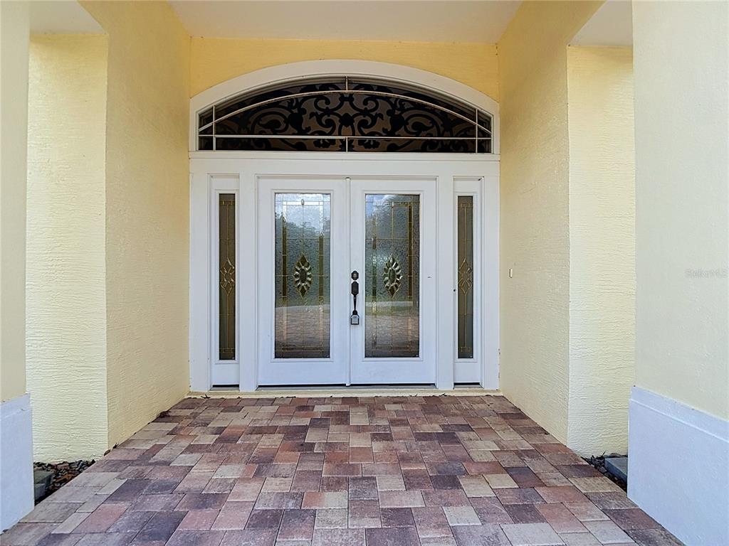 A double front door with glass inserts and an arched transom sits on a patio — 9433 WILDERNESS TRAIL, WEEKI WACHEE, FL