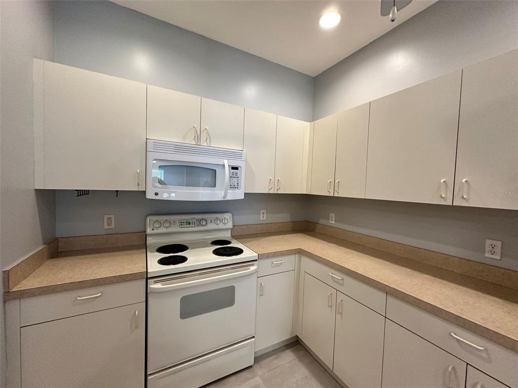 A kitchen features white cabinets, a white stove, a microwave, and tan laminate countertops — 1641 RED OAK LANE, PORT CHARLOTTE, FL
