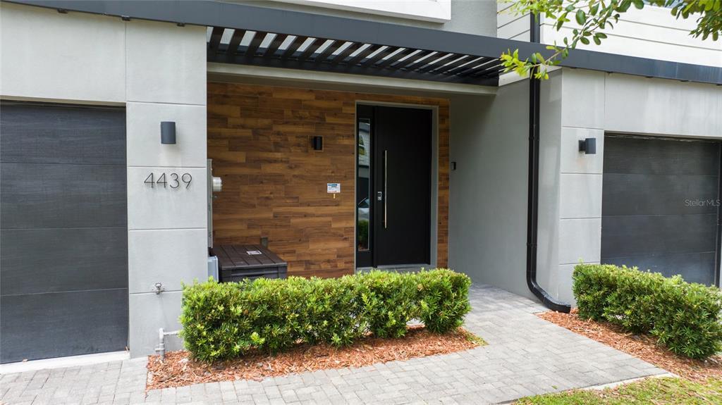 The exterior of a modern home features a wood-paneled entryway, two garages, and landscaping — 4439 LE REVE COURT, KISSIMMEE, FL