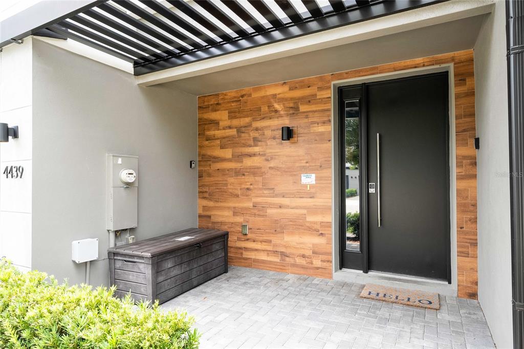 A modern entryway features a dark door, wood-look tile wall, and a gray storage bench — 4439 LE REVE COURT, KISSIMMEE, FL