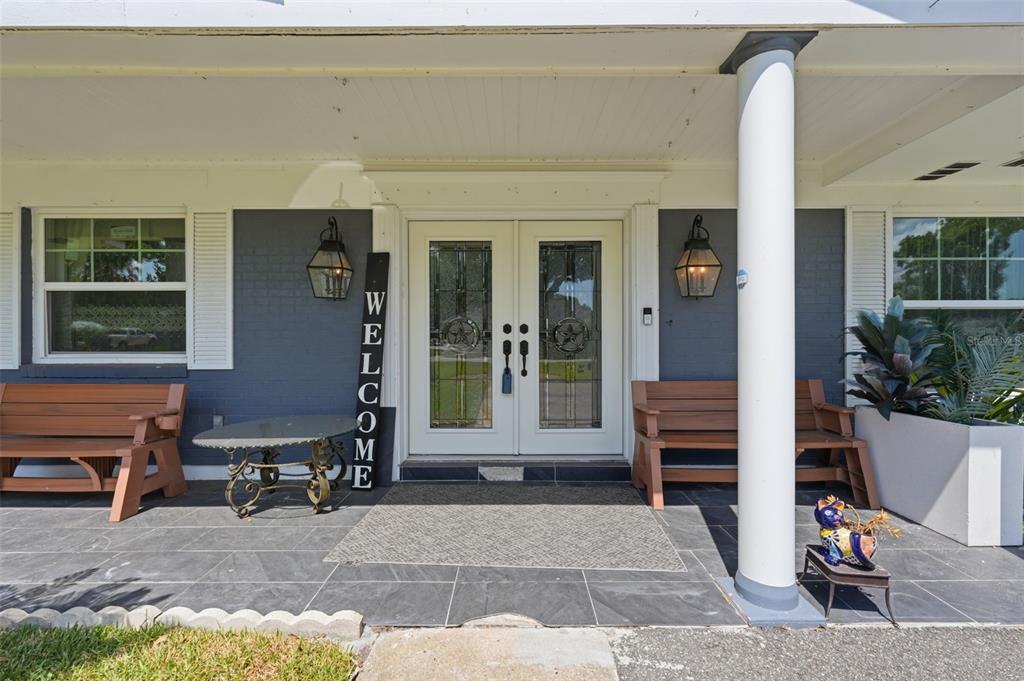 A covered front porch features a dark gray brick exterior, double glass doors, and wooden benches — 3678 E LAKE DRIVE, LAND O LAKES, FL
