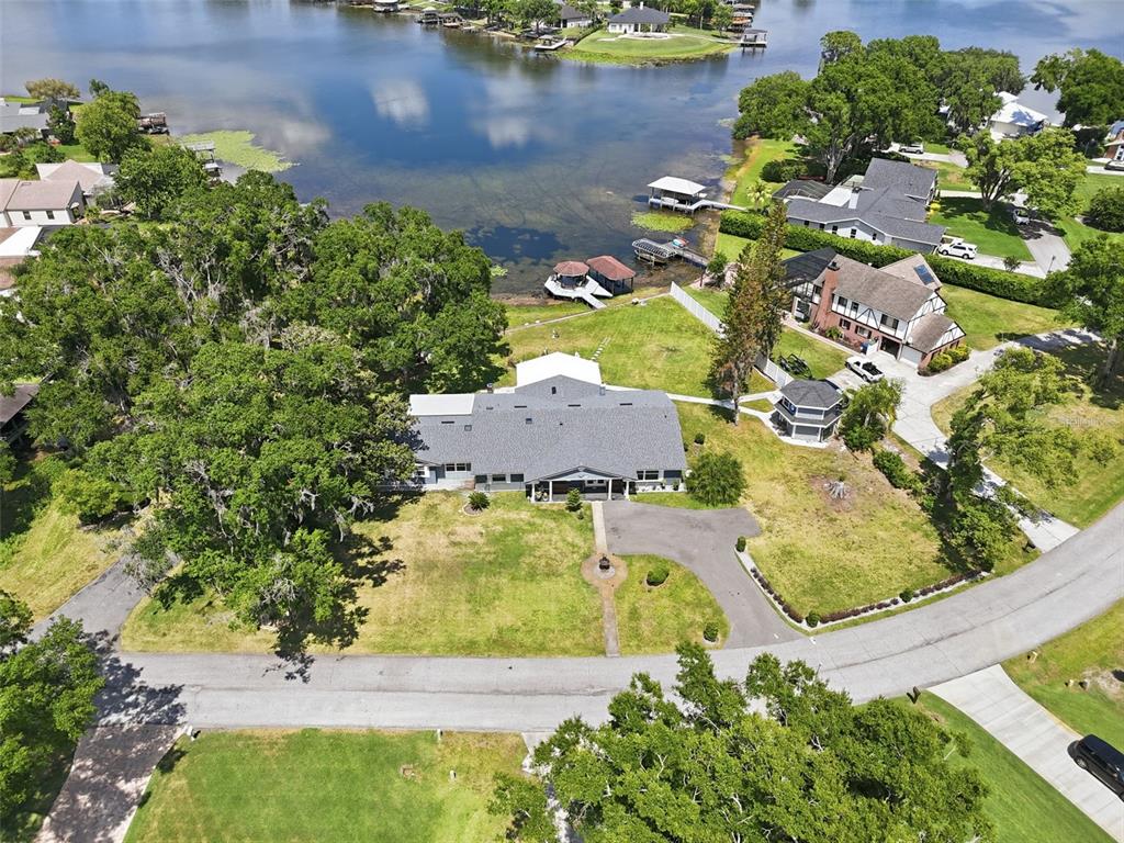 An aerial view shows a large house with a gray roof situated near a lake — 3678 E LAKE DRIVE, LAND O LAKES, FL
