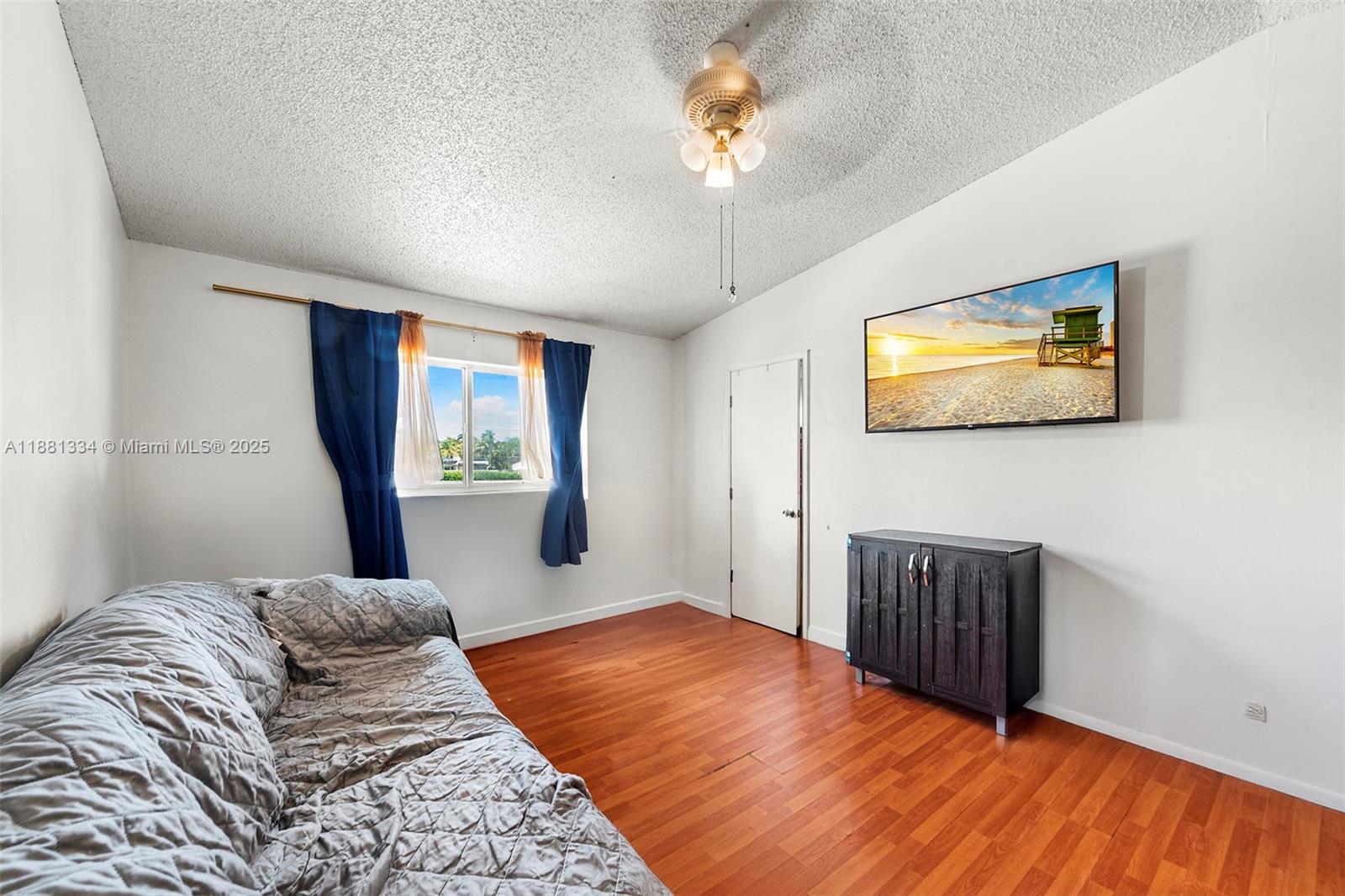 A bedroom features wood-look flooring, a ceiling fan, a window with curtains, and a television — 3630 N 56th Ave # 323, Hollywood FL 33021, HOLLYWOOD, FL