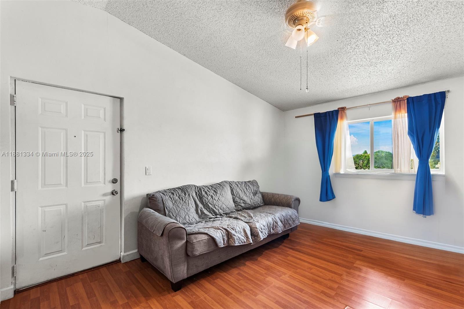 A living room features a gray sofa, wood-look flooring, a ceiling fan, and a window — 3630 N 56th Ave # 323, Hollywood FL 33021, HOLLYWOOD, FL