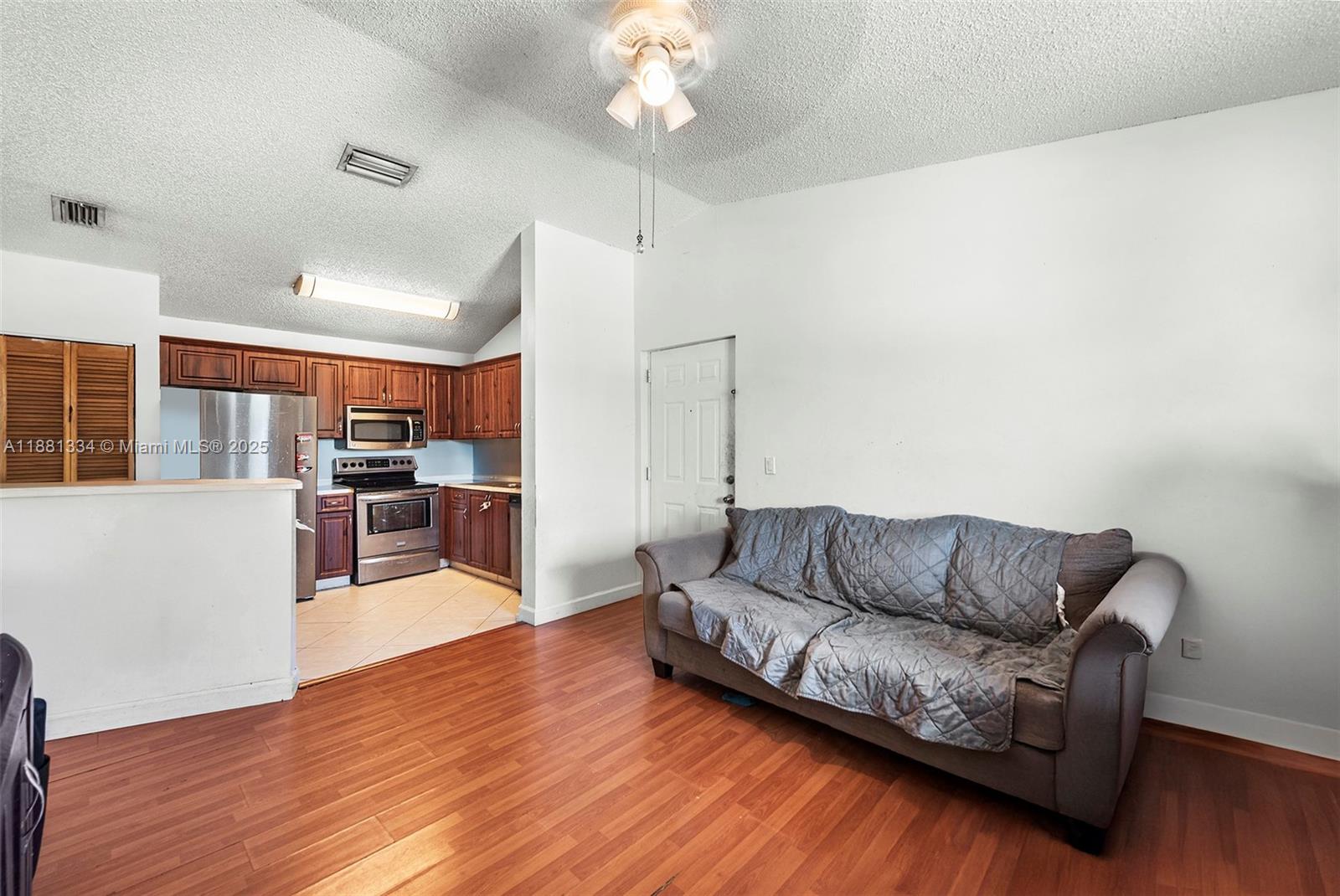 A living room with wood flooring and a sofa sits adjacent to a kitchen area — 3630 N 56th Ave # 323, Hollywood FL 33021, HOLLYWOOD, FL