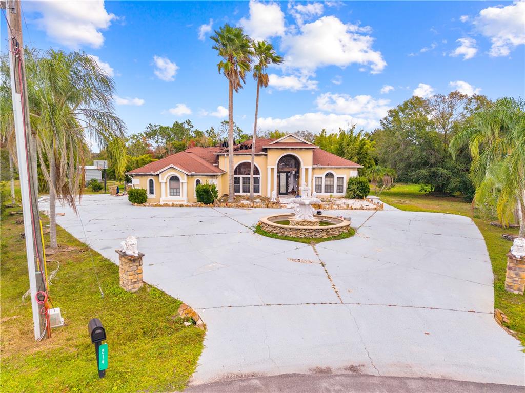 A large, single-story house with a circular driveway and fountain shows significant fire damage — 214 TARANTO WAY, KISSIMMEE, FL