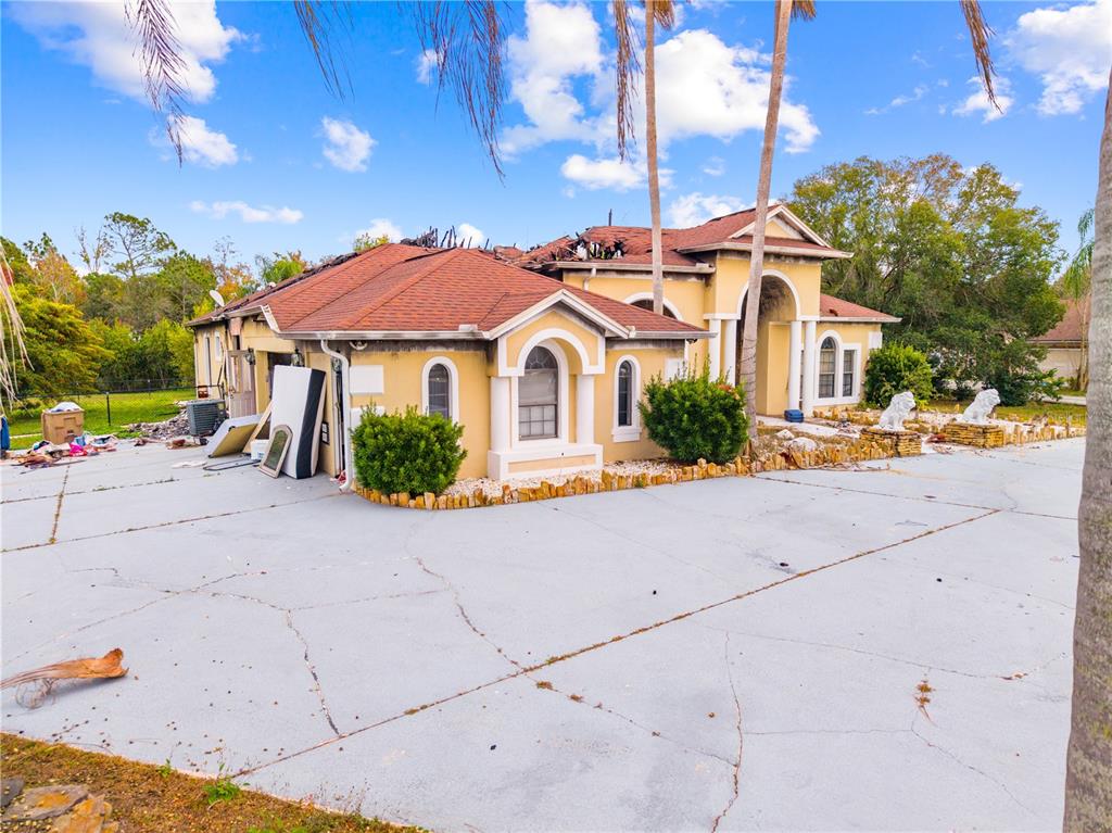 A yellow house with a damaged roof and debris in the yard — 214 TARANTO WAY, KISSIMMEE, FL